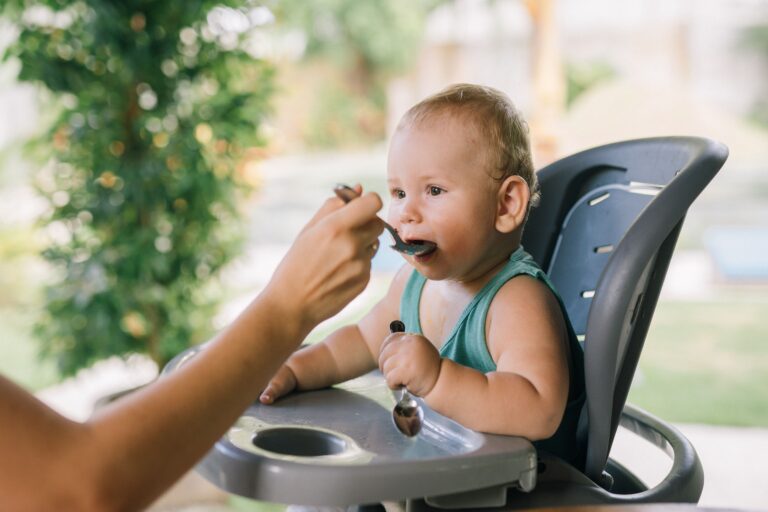 Baby being fed while sitting in a high chair outdoors