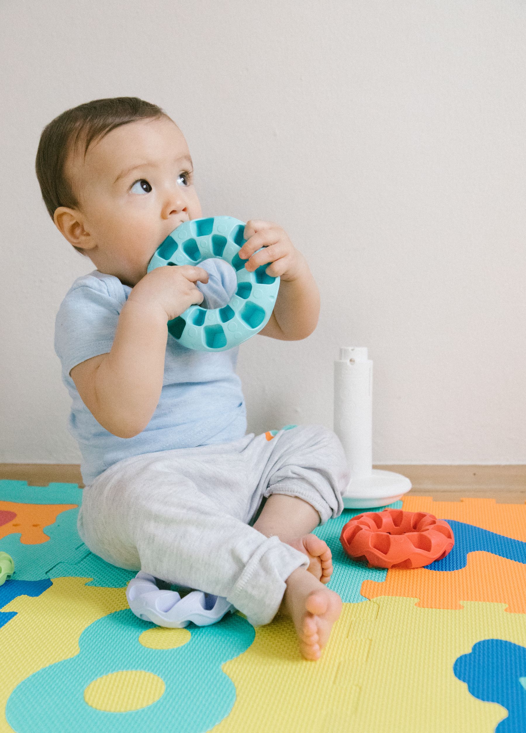 Baby sitting on a colourful puzzle mat with toys indoors